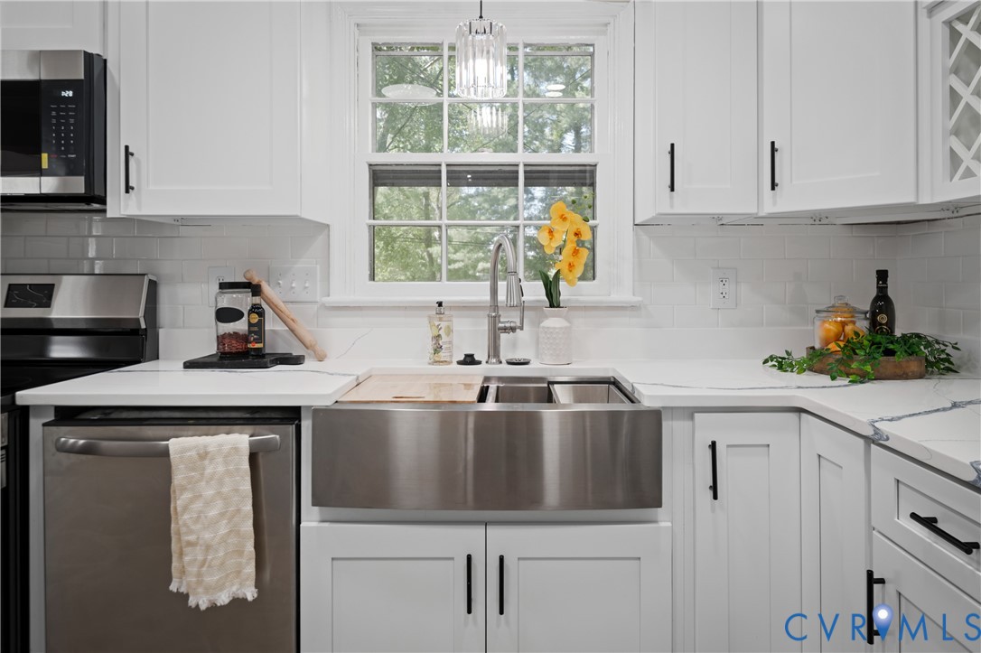White cabinetry featuring black hardware, stainless steel farmhouse sink with gooseneck faucet, light-toned countertops, subway tile backsplash, and built-in stainless steel appliances