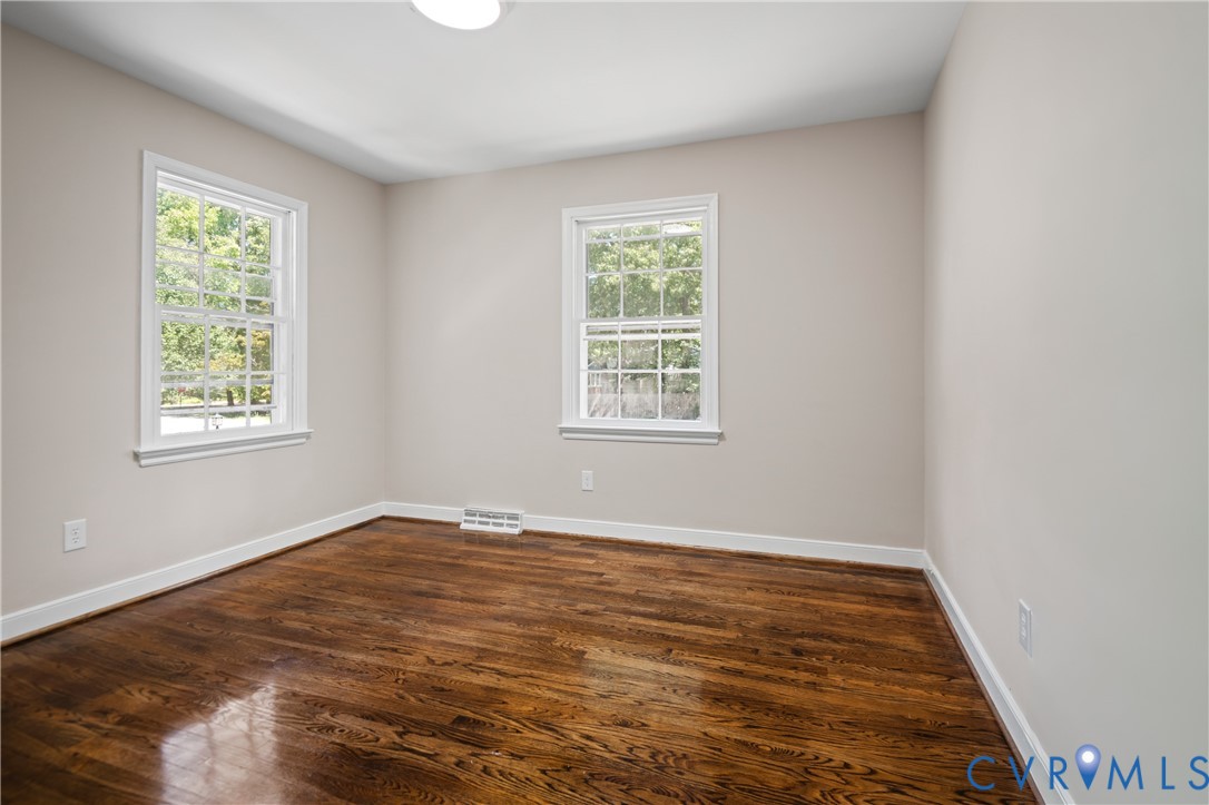 Neutral-toned interior room featuring wood-finish flooring and two double-hung windows with grid detailing