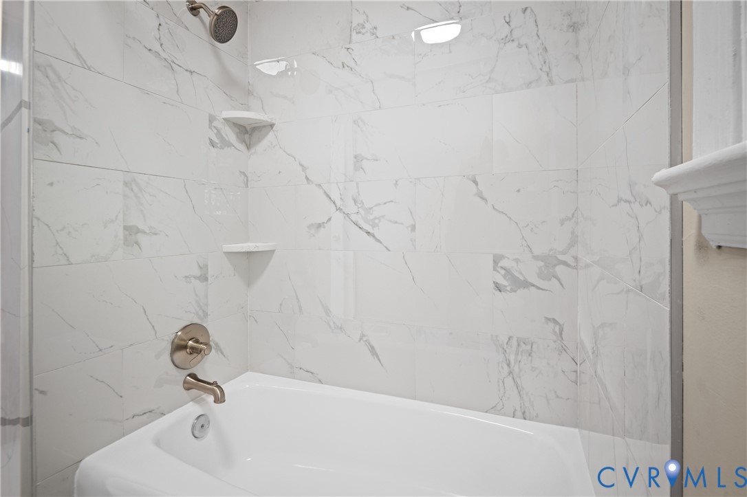 Full-height wall tiling with a veined pattern, integrated corner shelving, polished metal shower fixtures, and a porcelain soaking tub