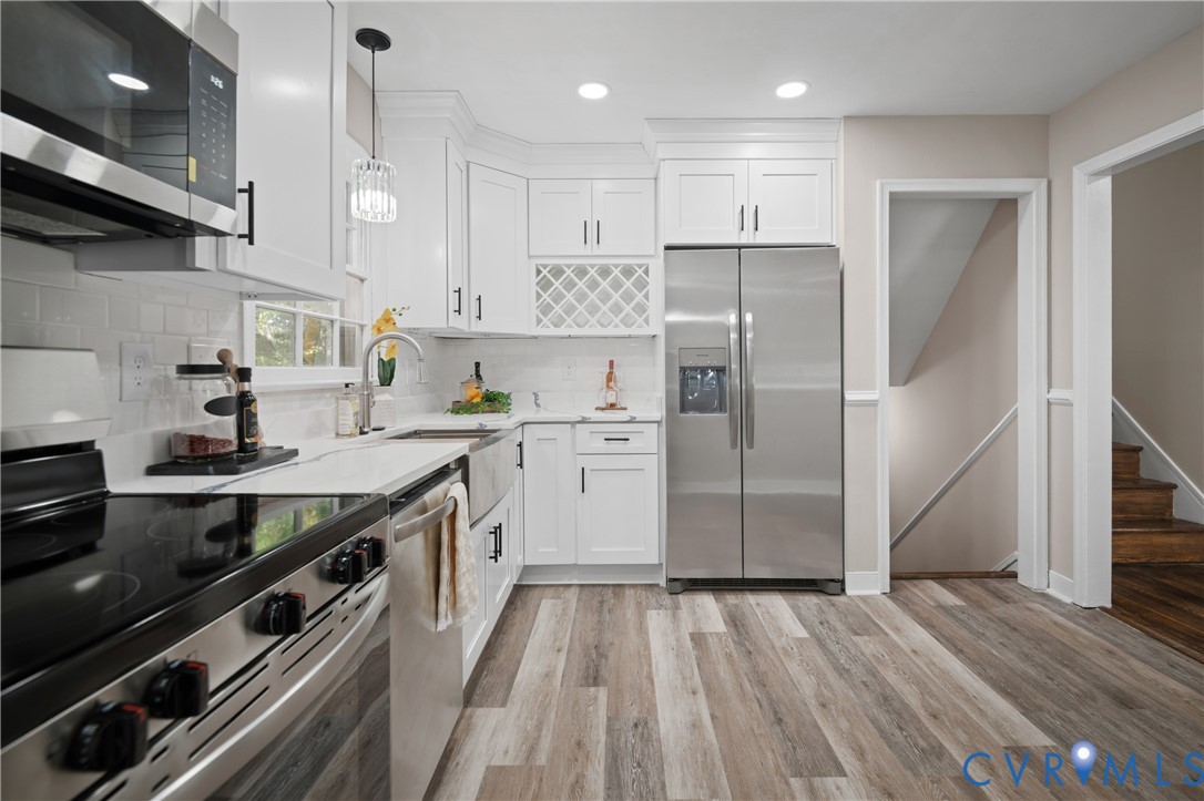 Kitchen featuring white shaker cabinetry, stainless steel appliances, subway tile backsplash, apron-front sink, and wood-finish flooring