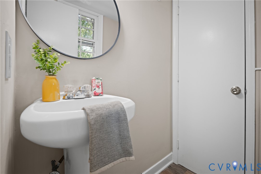 Corner-mounted pedestal sink featuring a chrome dual-handle faucet, oval wall-mounted mirror, and wood-finish flooring