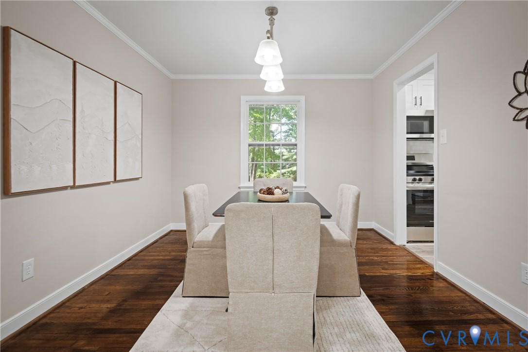 Dining area featuring dark wood-finish flooring, crown molding, and a three-light pendant fixture