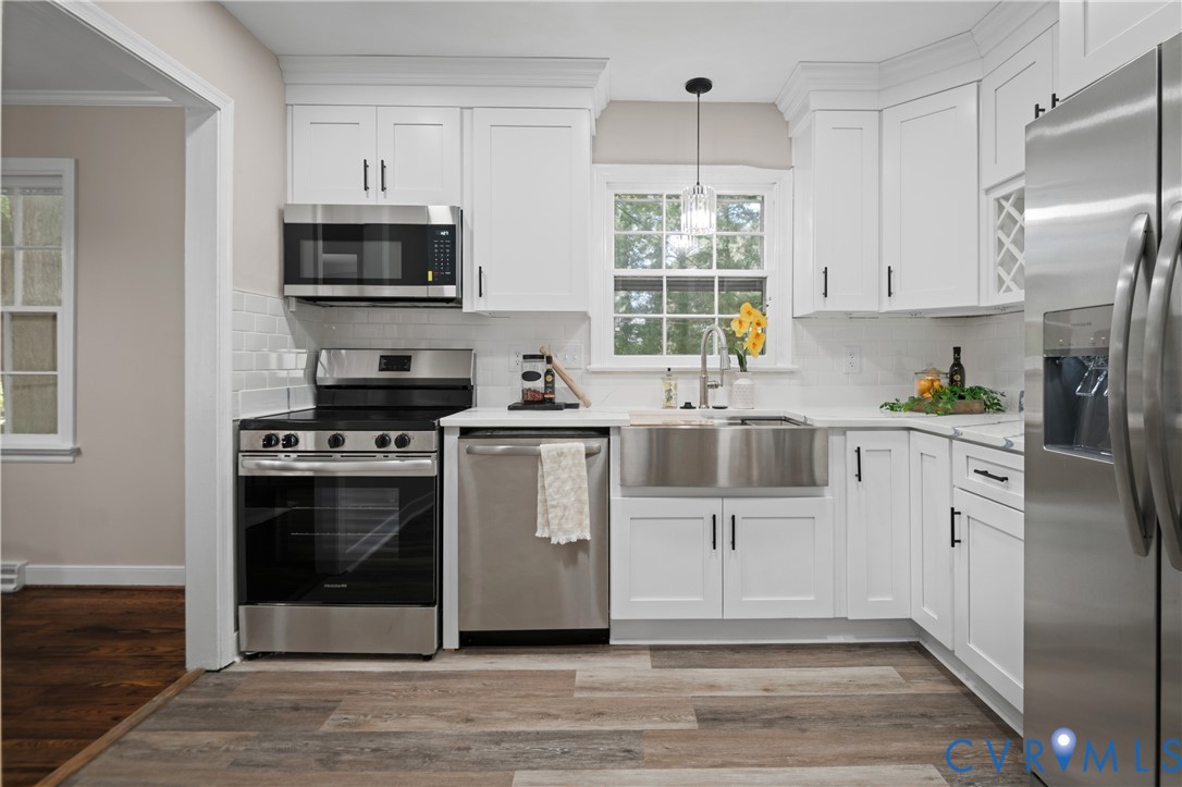 Kitchen featuring white shaker-style cabinetry, stainless steel farmhouse sink, white subway tile backsplash, stainless steel appliances, and wood-finish flooring
