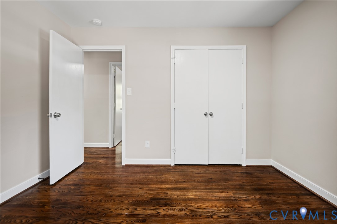 Room featuring dark wood-finish flooring, neutral walls, and dual-door closet with spherical knobs