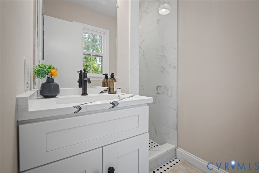 White vanity with an integrated basin and stone-patterned countertop featuring a matte black faucet, paired with a shower enclosure showcasing large-format surround tile and a geometric mosaic floor