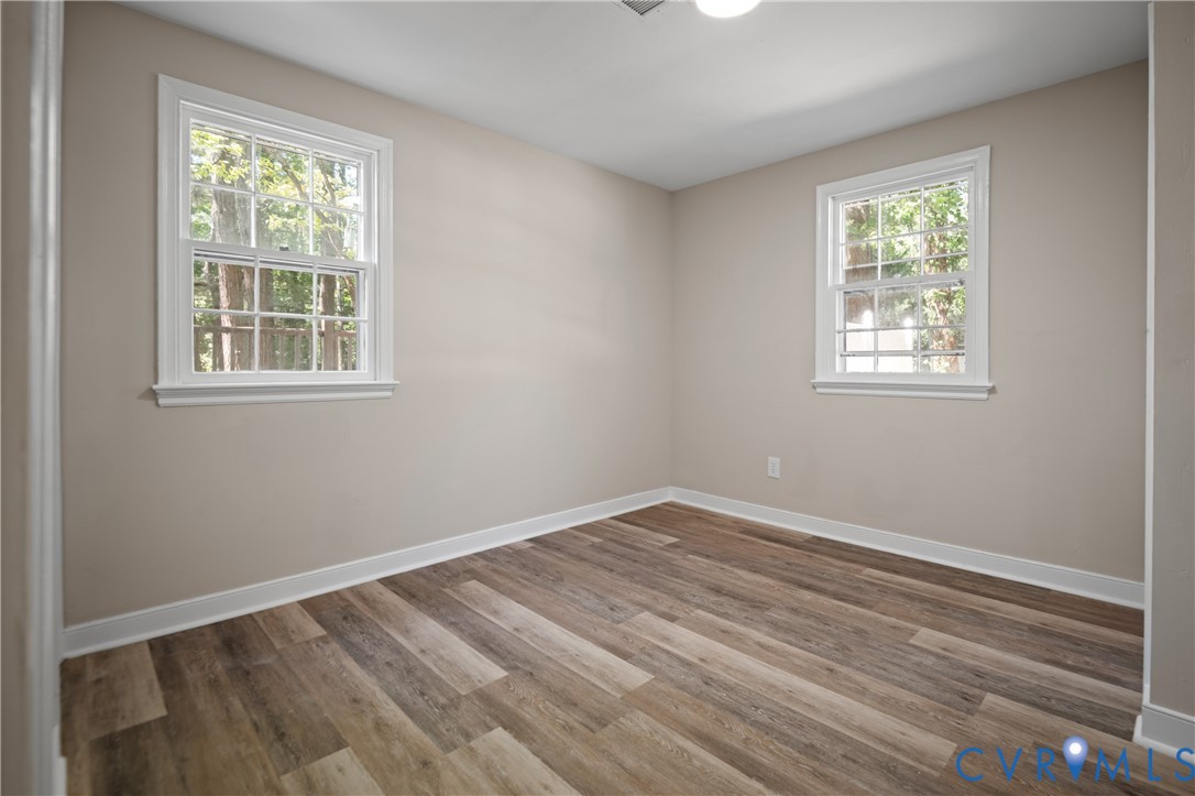 Neutral-toned interior space featuring wood-finish flooring, two double-hung windows with muntins, and a ceiling-mounted light fixture