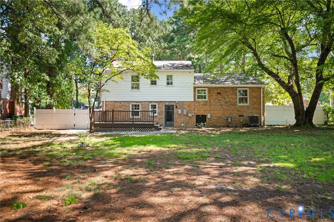 Rear exterior featuring a brick and white siding faade, elevated wood deck, and white privacy fencing on a wooded lot