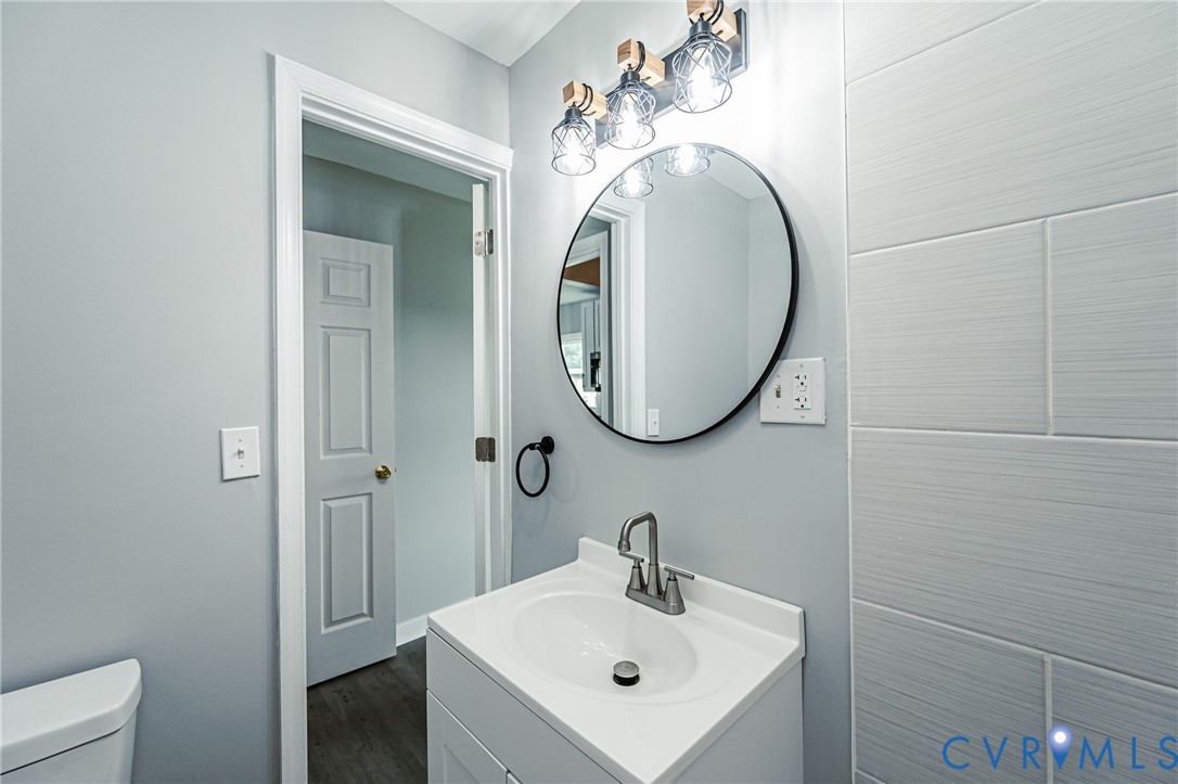 Bathroom vanity featuring a solid-surface integrated sink, circular black-framed mirror, three-light industrial-style fixture, and horizontal textured wall tiling