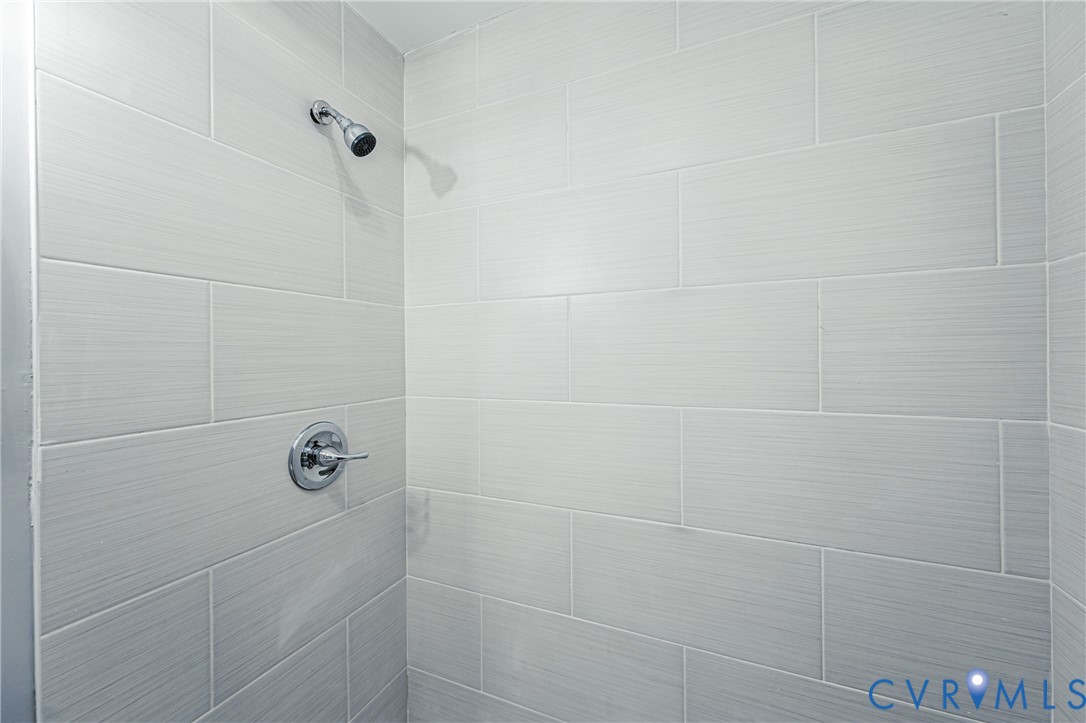 Shower enclosure featuring large-format light-toned textured wall tile, chrome shower head, and matching chrome pressure-balance valve trim