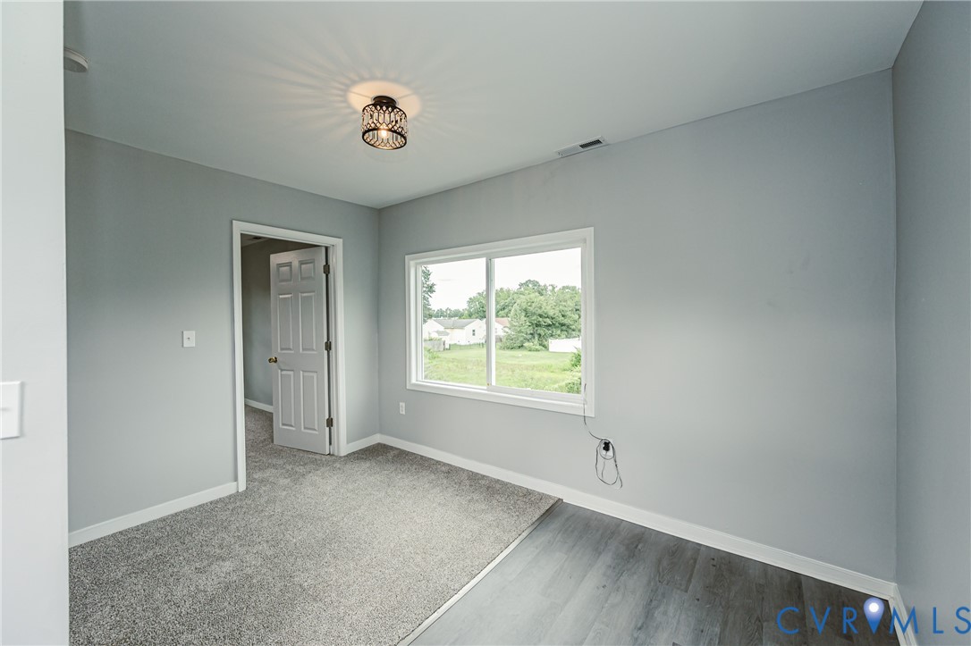 Interior room featuring neutral-tone paint, wall-to-wall carpeting, wood-finish flooring, a six-panel door, and a geometric semi-flush mount light fixture