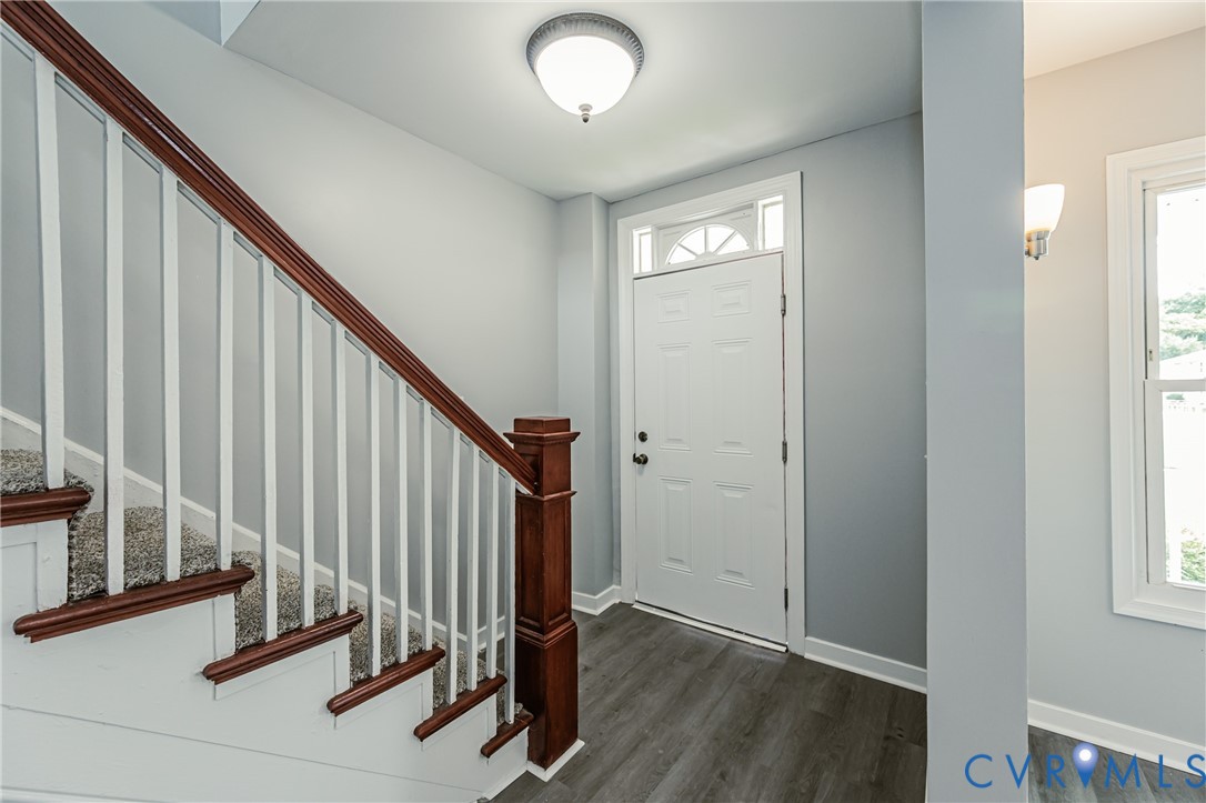 Entryway featuring wood-finish flooring, a staircase with a wooden handrail, white balusters, a paneled door with an arched transom window, and a flush-mount light fixture