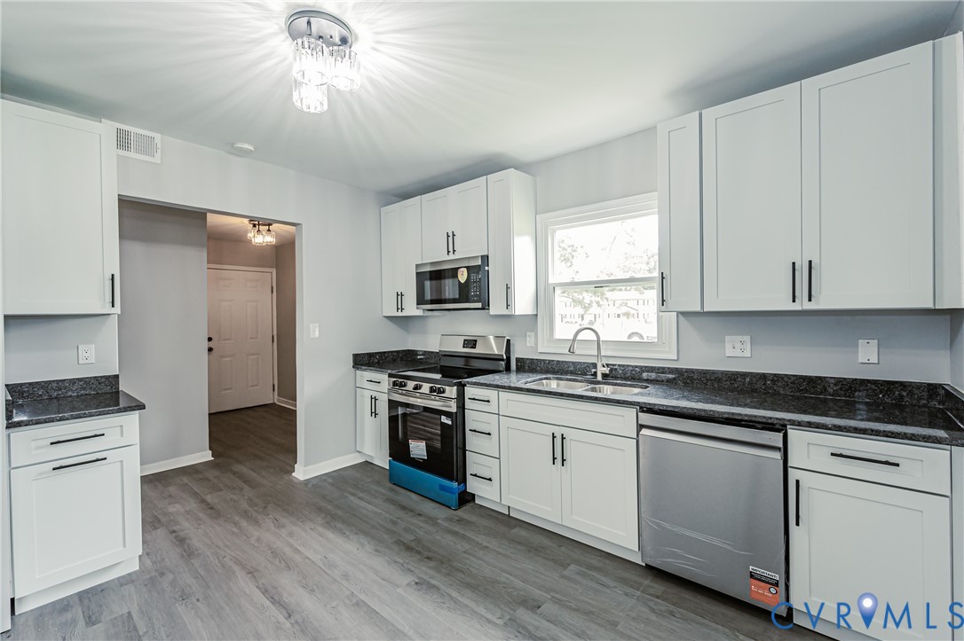 Kitchen featuring white shaker-style cabinetry, dark stone-finish countertops, stainless steel appliances, and wood-finish flooring