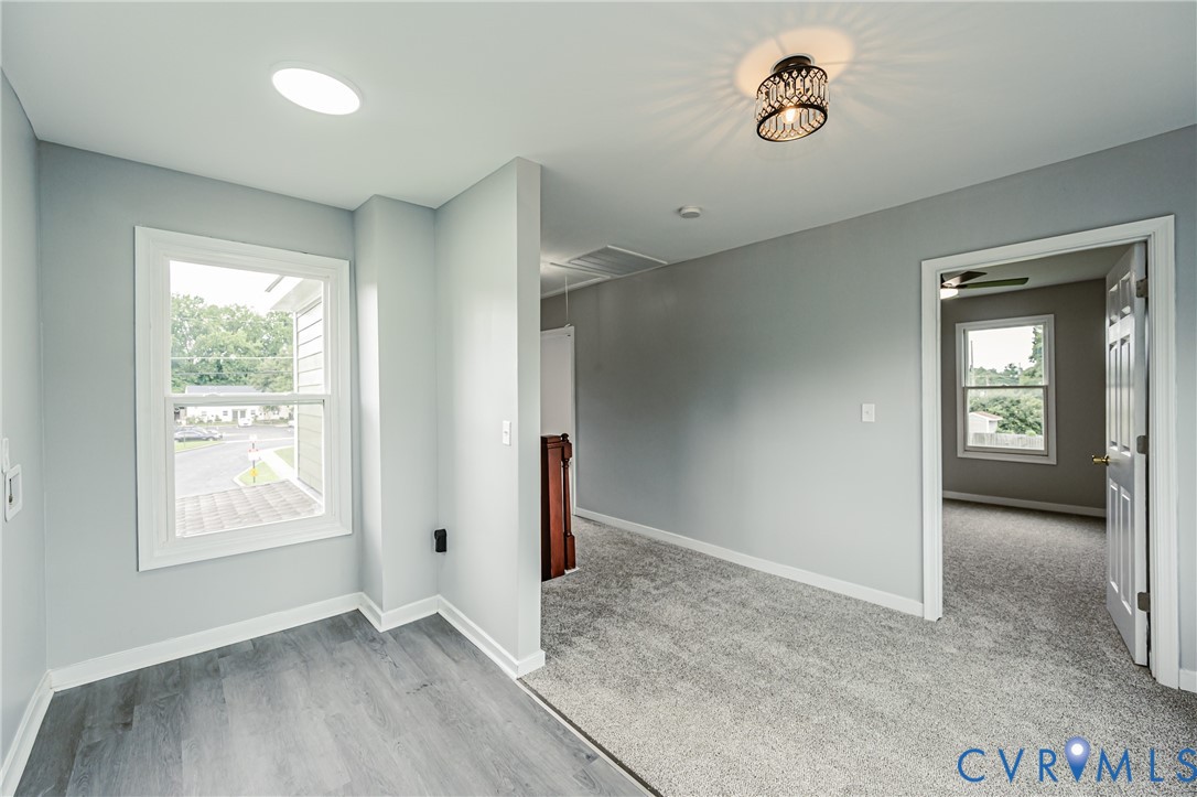 Neutral-toned interior featuring wood-finish flooring, wall-to-wall carpeting, a decorative metal semi-flush mount light fixture, and a white double-hung window