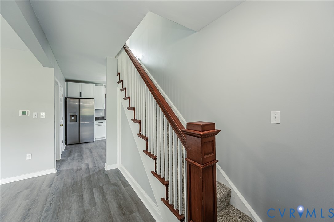 Staircase featuring a stained wood handrail, decorative newel post, and white balusters, accented by wood-finish flooring and integrated stainless steel refrigerator