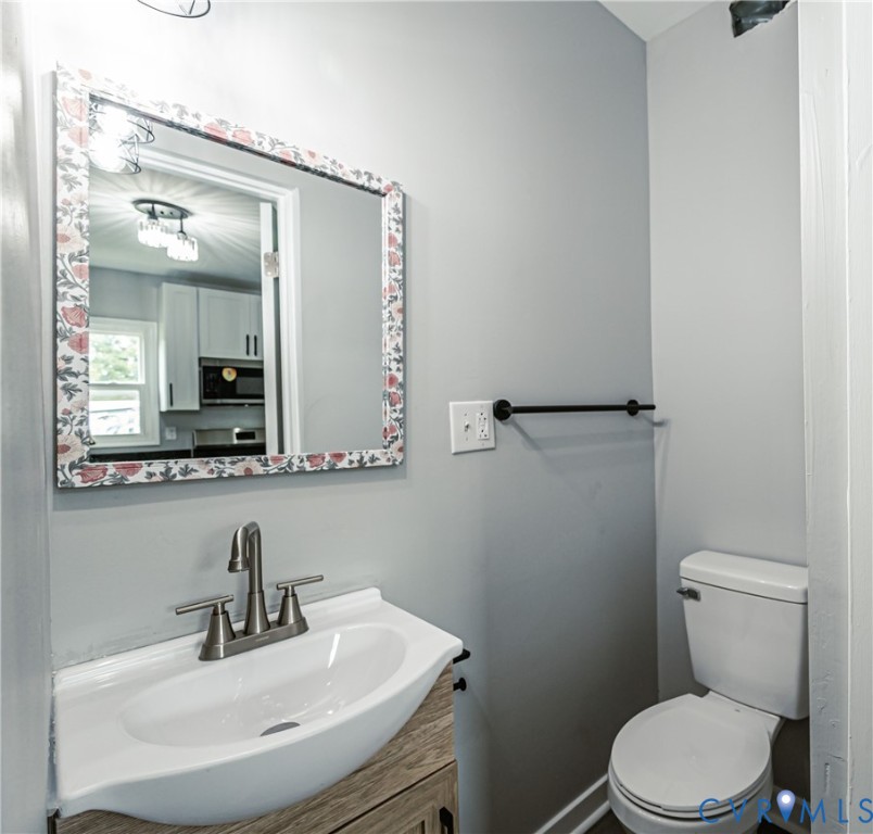 Wall-mounted vanity featuring a white basin, wood-finish cabinetry, brushed nickel faucet, and a matte black towel bar