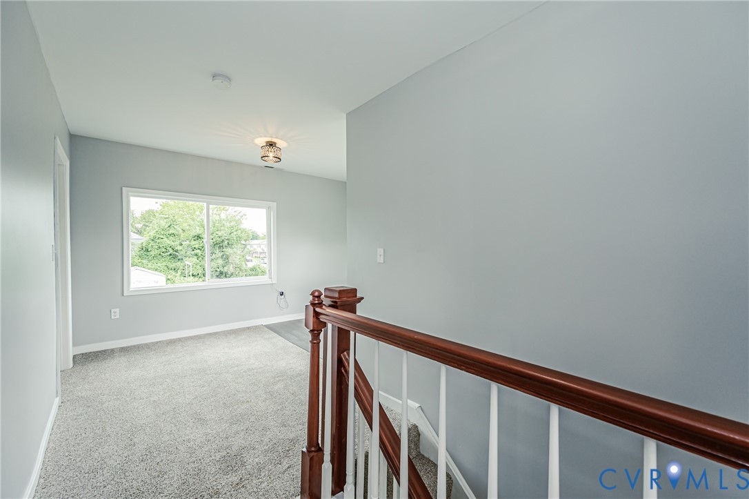 Staircase featuring a polished wood handrail with white balusters, neutral carpeting, and a flush-mount light fixture