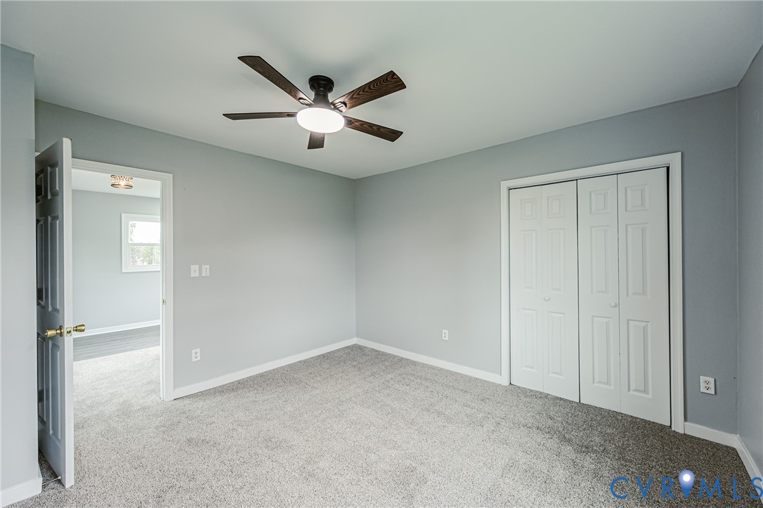 Neutral-toned wall paint, carpeted flooring, multi-panel closet doors, and a ceiling fan with integrated lighting
