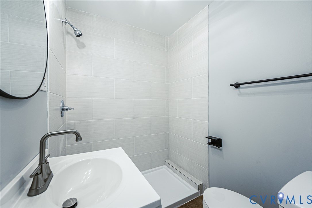 Bathroom featuring a white pedestal sink with a metallic faucet, a walk-in shower with floor-to-ceiling tile surround, and a circular wall-mounted mirror