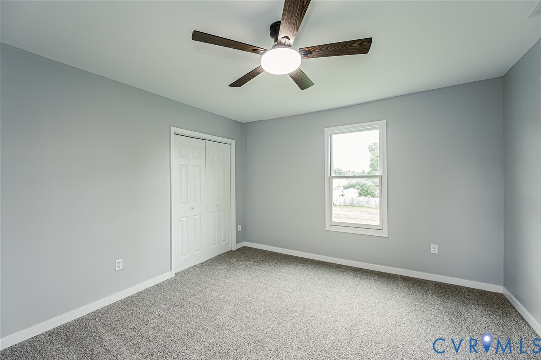 Neutral-toned wall paint, wall-to-wall carpeting, ceiling fan with integrated lighting, and dual-panel closet doors