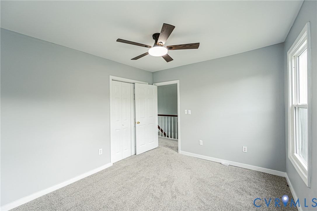 Neutral wall-toned room featuring plush carpeting, a multi-blade ceiling fan with integrated lighting, and white six-panel closet doors