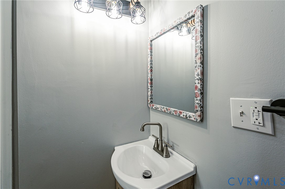 Wall-mounted vanity featuring a white basin, brushed metal faucet, framed mirror, and triple-light overhead fixture
