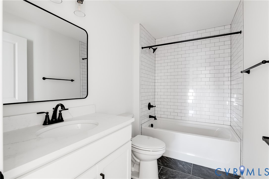 Bathroom featuring a white vanity with a solid-surface countertop, rectangular mirror with a black frame, subway-tiled shower surround, matte black hardware, and dark stone-finish flooring