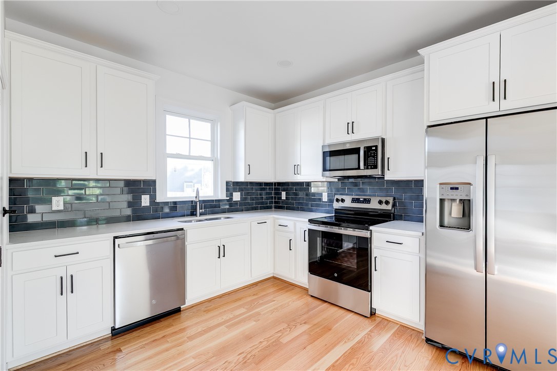 Kitchen featuring white cabinetry, dark tile backsplash, wood-finish flooring, and stainless steel appliances