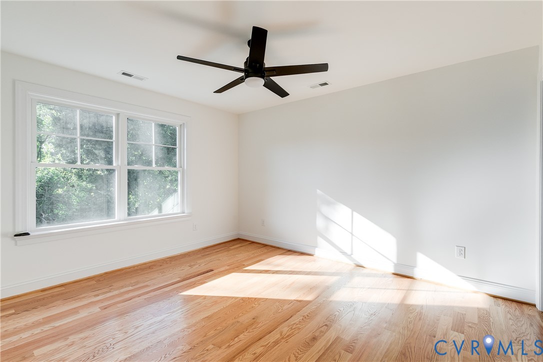 Interior space featuring wood-finish flooring, a matte black multi-blade ceiling fan with integrated lighting, and a double-hung window with muntins