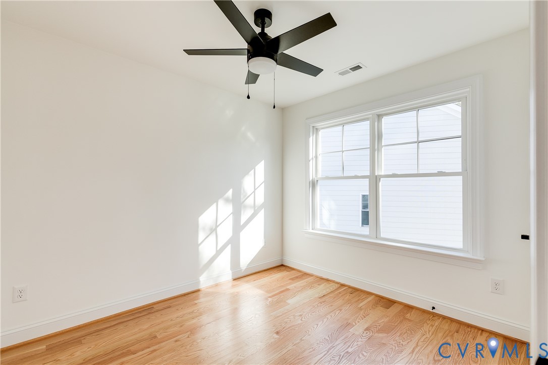 Room featuring wood-finish flooring, a matte black ceiling fan with an integrated light fixture, and double-hung windows with muntin bars