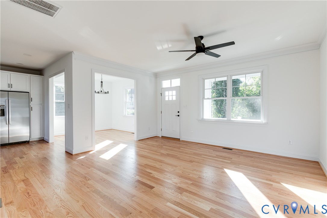 Open interior featuring wood-finish flooring, white cabinetry, a multi-pane door with transom, large windows, and a matte black ceiling fan