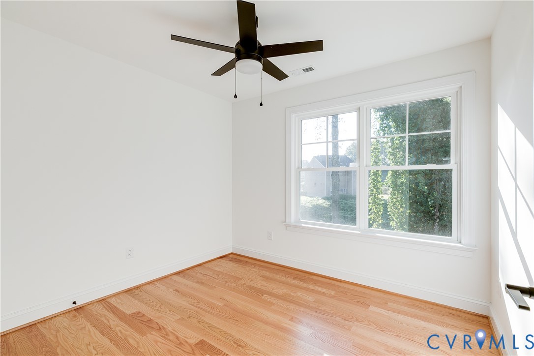 Room featuring wood-finish flooring, white walls, double-pane window with grid muntins, and a ceiling-mounted fan with integrated light