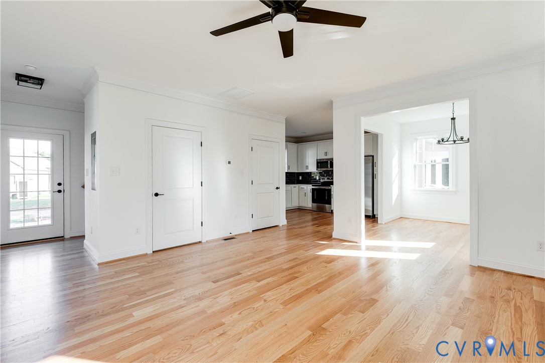 Open interior space featuring light wood-finish flooring, white paneled doors, a ceiling fan with integrated lighting, and a multi-pane glass entry door