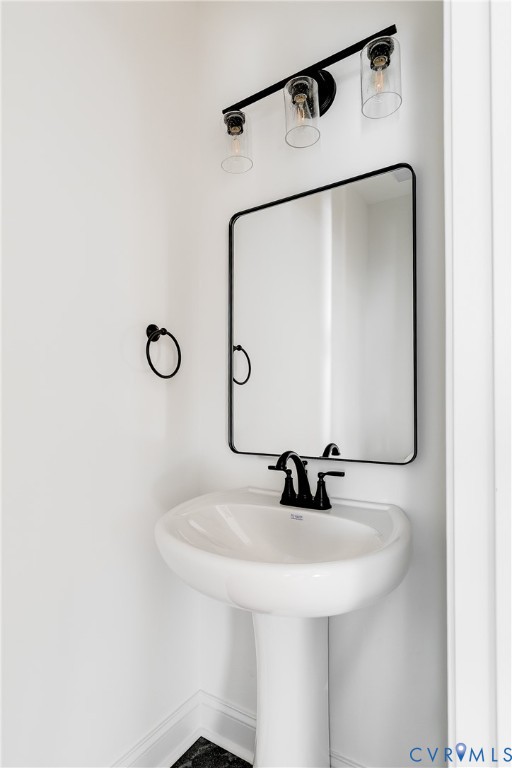 White porcelain pedestal sink with a matte black widespread faucet, rectangular mirror with a matte black frame, and a three-light vanity fixture featuring clear glass cylindrical shades