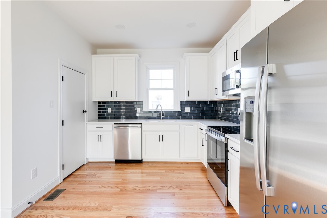 Kitchen featuring white shaker-style cabinetry, stainless steel appliances, dark subway tile backsplash, light wood-finish flooring, and a single-basin sink with a gooseneck faucet