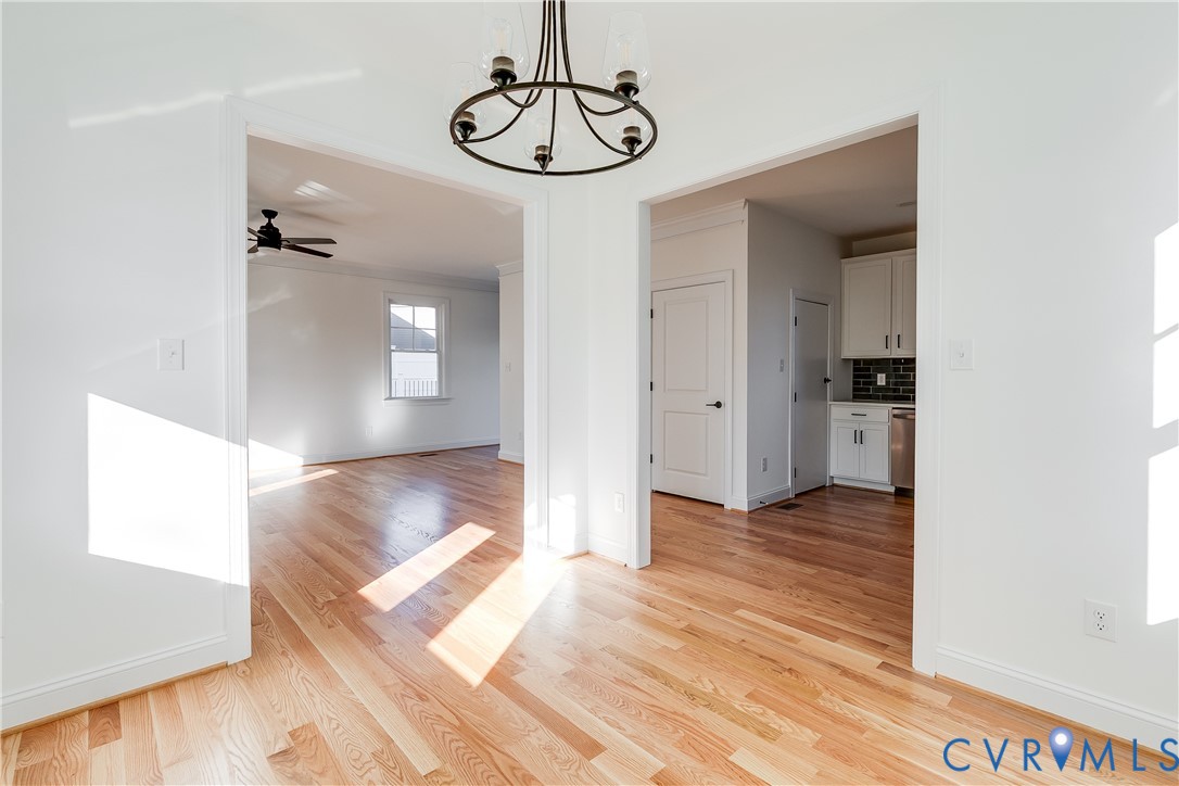 Wood-finish flooring, matte black five-light chandelier, recessed interior doorways, and white shaker-style cabinetry with tile backsplash