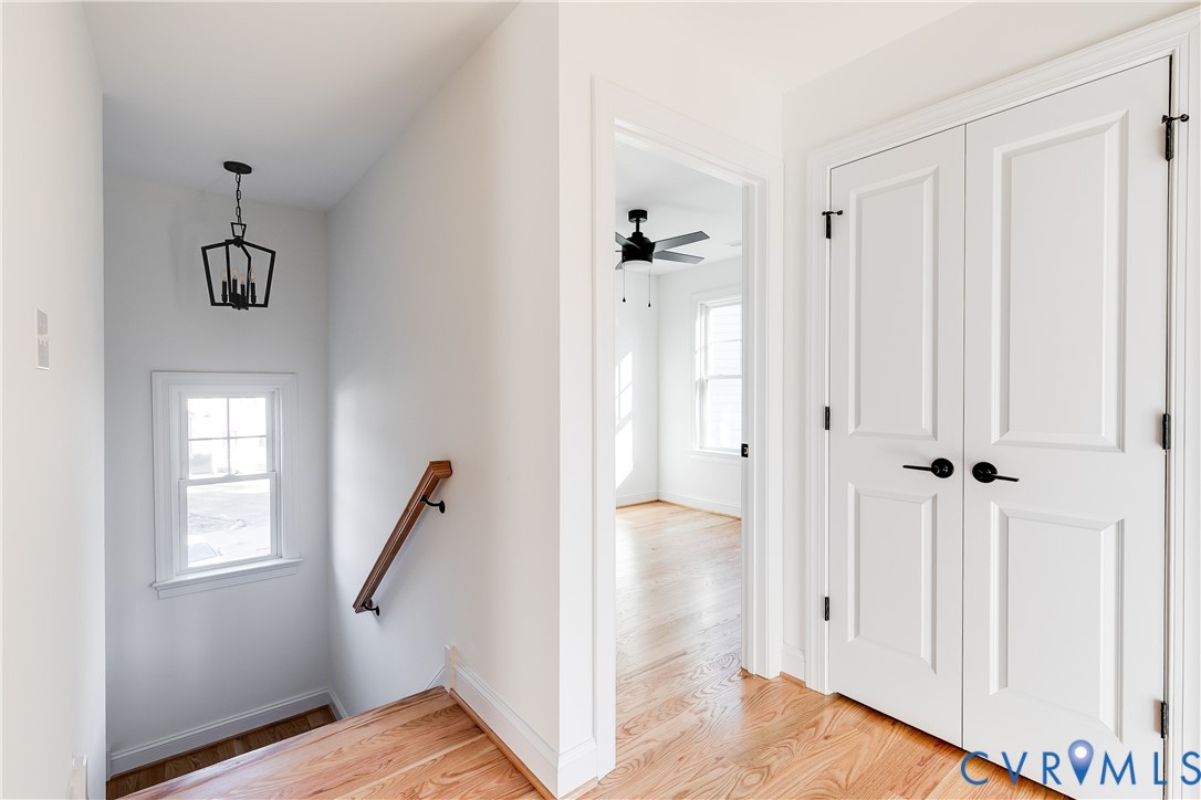 Wood-finish flooring, white paneled double doors with matte black hardware, wooden handrail, and geometric metal pendant lighting
