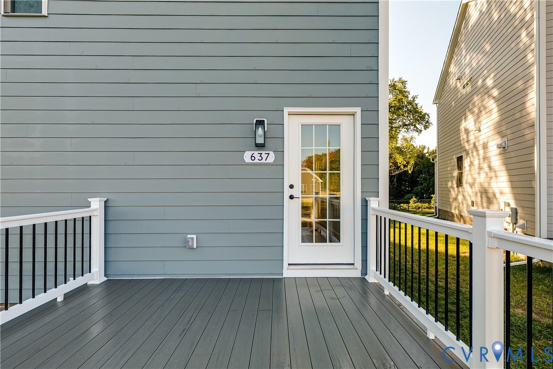 Composite deck featuring white railings with vertical black balusters, lap siding exterior, and a multi-pane glass entry door with a wall-mounted light fixture