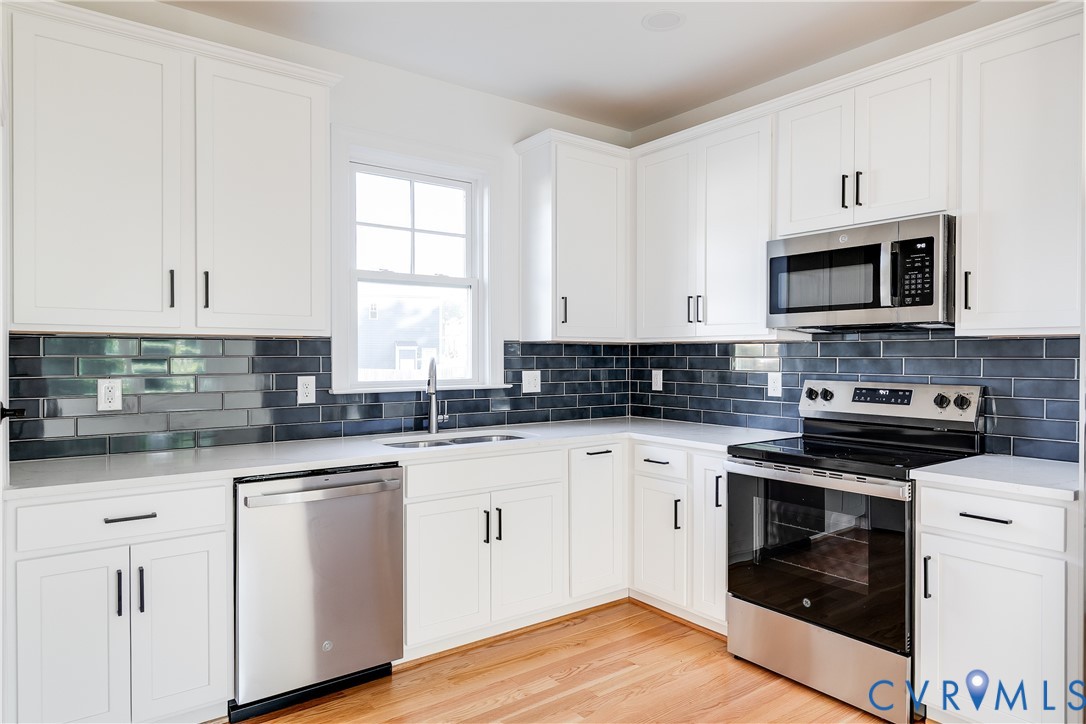 Kitchen featuring white shaker-style cabinetry, dark subway tile backsplash, solid-surface countertops, stainless steel appliances, and wood-finish flooring