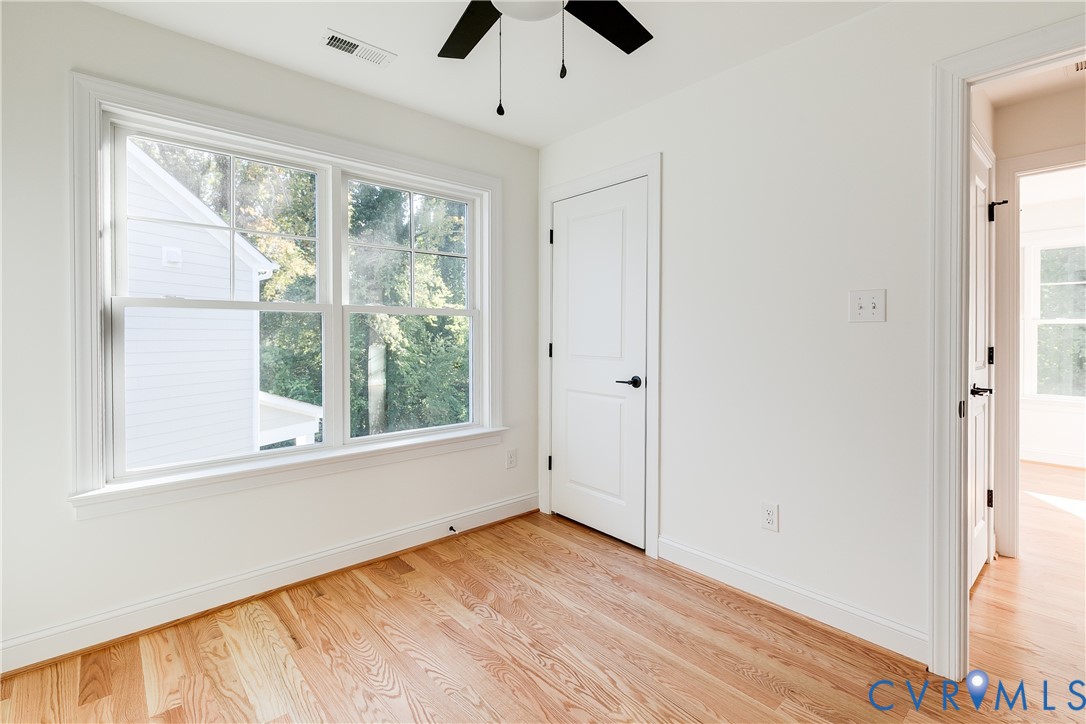 Wood-finish flooring, multi-pane window with grid detailing, matte black door hardware, and a ceiling fan