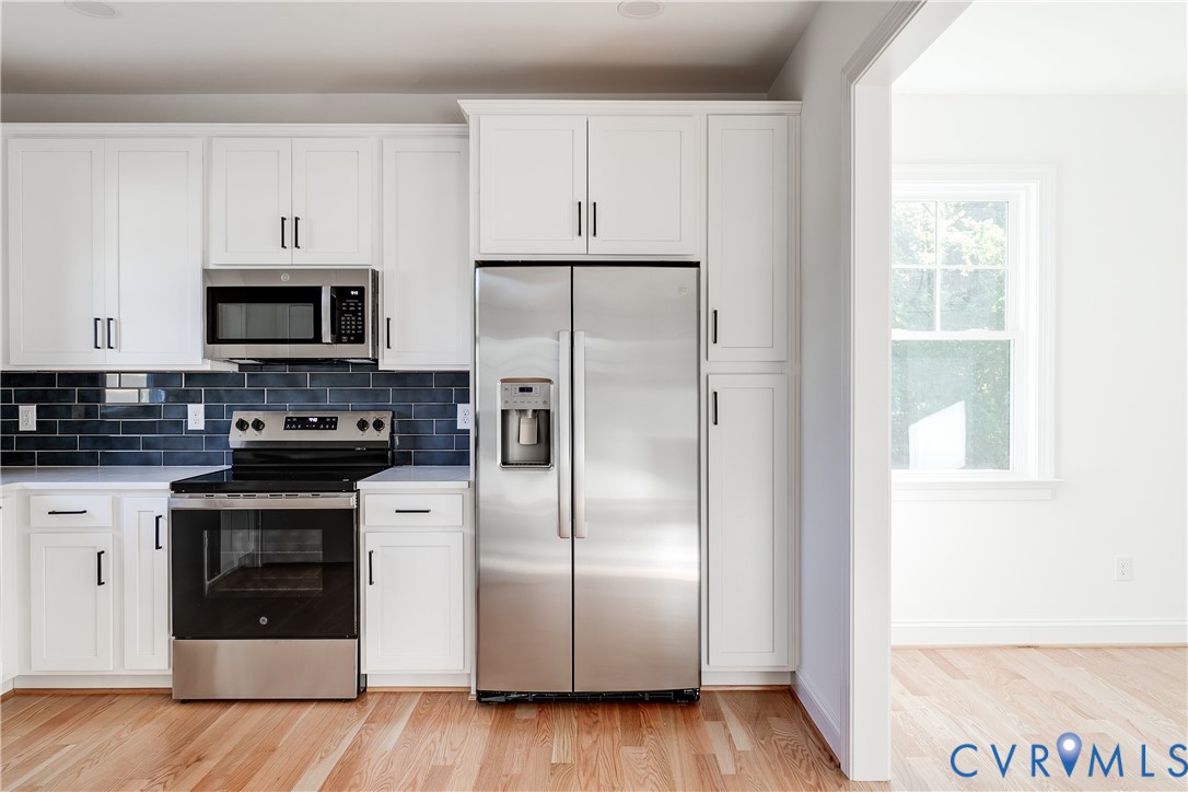 Kitchen featuring white cabinetry with matte black hardware, stainless steel appliances, dark subway tile backsplash, and wood-finish flooring