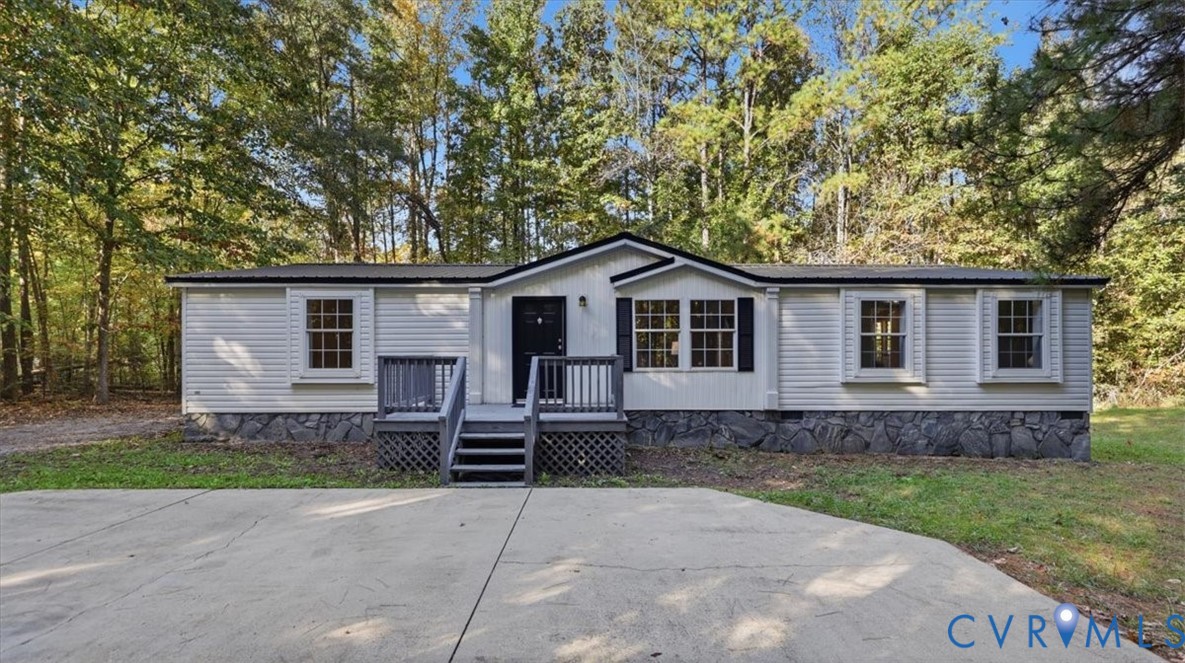 Light-colored siding exterior featuring a stone-veneer foundation, black window shutters, a front porch with railing, and an expansive concrete parking pad