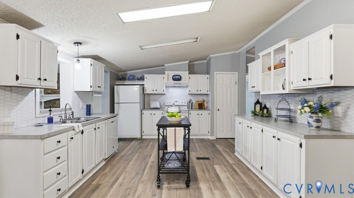 Kitchen featuring white shaker-style cabinetry, wood-finish flooring, hexagonal tile backsplash, solid-surface countertops, and built-in glass-front display cabinets