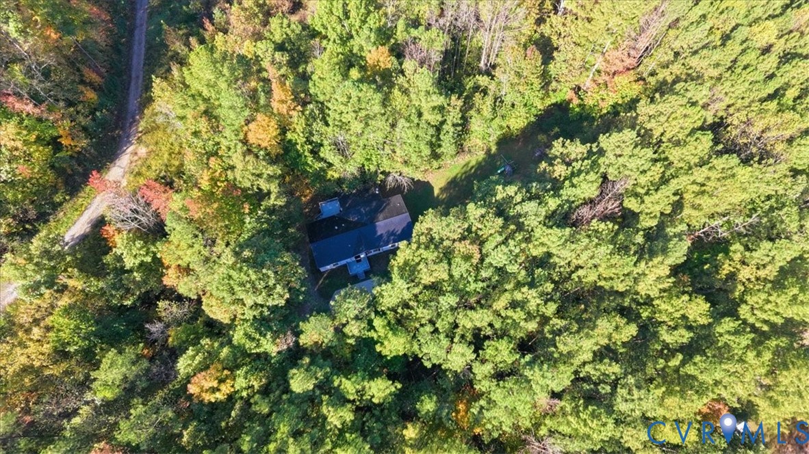 Aerial perspective of a detached residence nestled within a densely wooded lot, featuring a shingled roof and a private gravel drive
