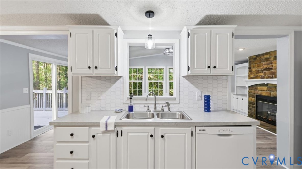 Kitchen featuring white cabinetry, a dual-basin stainless steel sink with a pull-down faucet, a hexagonal tile backsplash, and an integrated dishwasher Kitchen featuring white cabinetry, a dual-basin stainless steel sink with a pull-down faucet, a hexagonal tile backsplash, and an integrated dishwasher