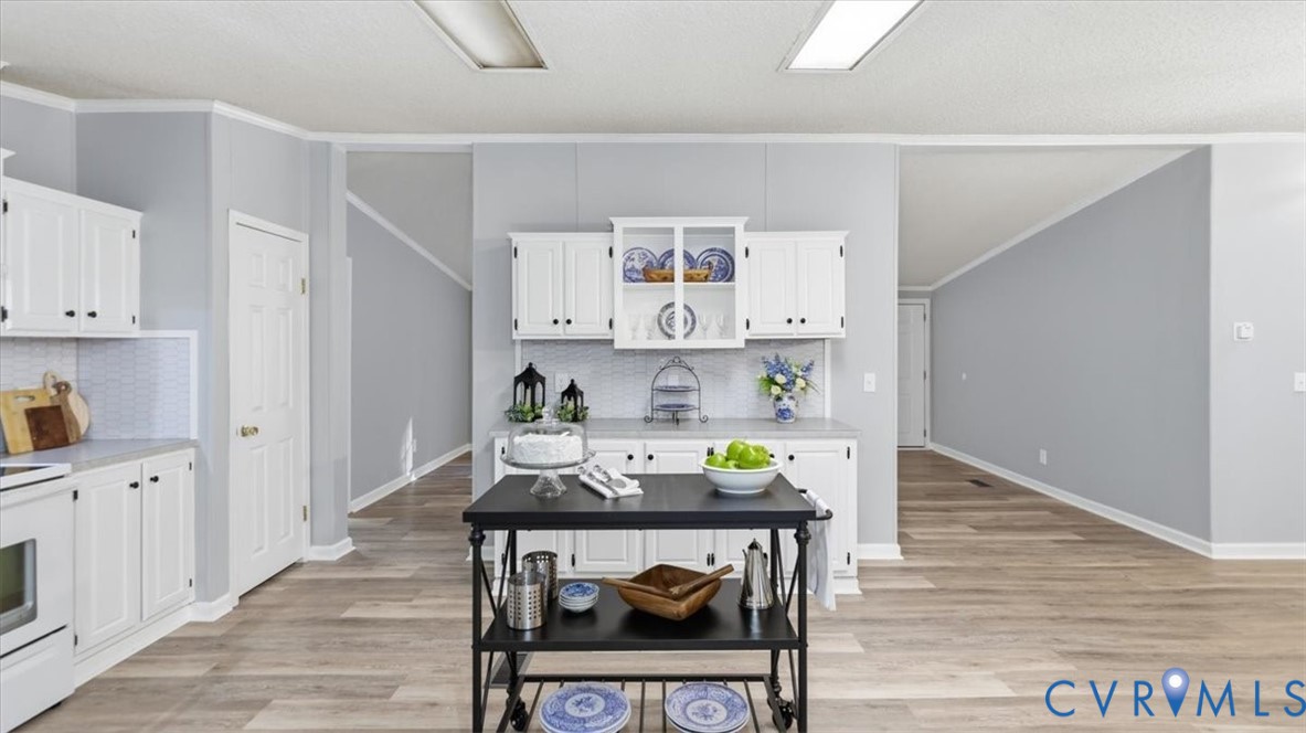 Kitchen featuring white cabinetry with glass-front display shelving, neutral solid-surface countertops, wood-finish flooring, and recessed ceiling lighting