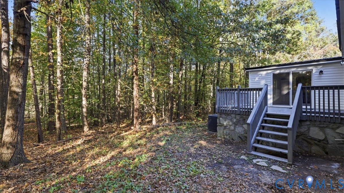 Rear exterior featuring a raised wooden deck with balustrades, stone foundation detailing, and sliding glass entry