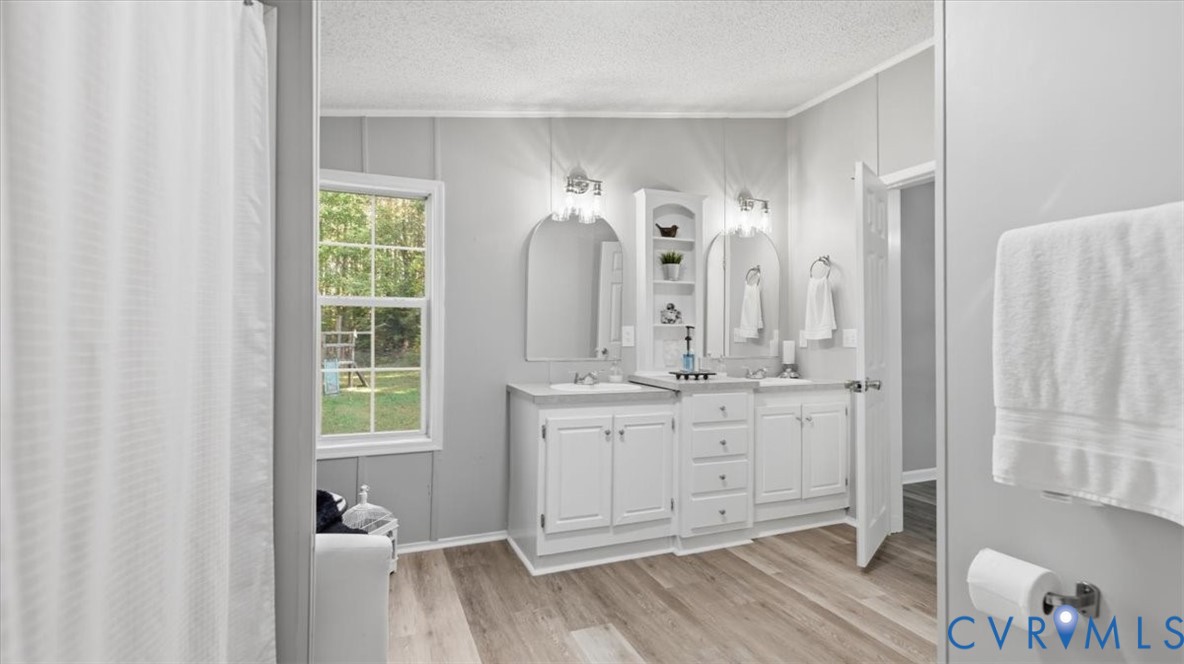 Double vanity with white cabinetry, central tower shelving, two arched wall mirrors, and wood-finish flooring
