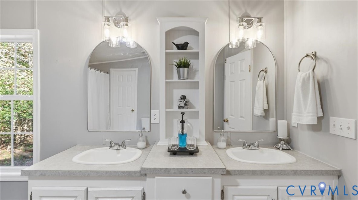 Double vanity featuring dual arched mirrors, integrated shelving, white cabinetry, and brushed nickel fixtures