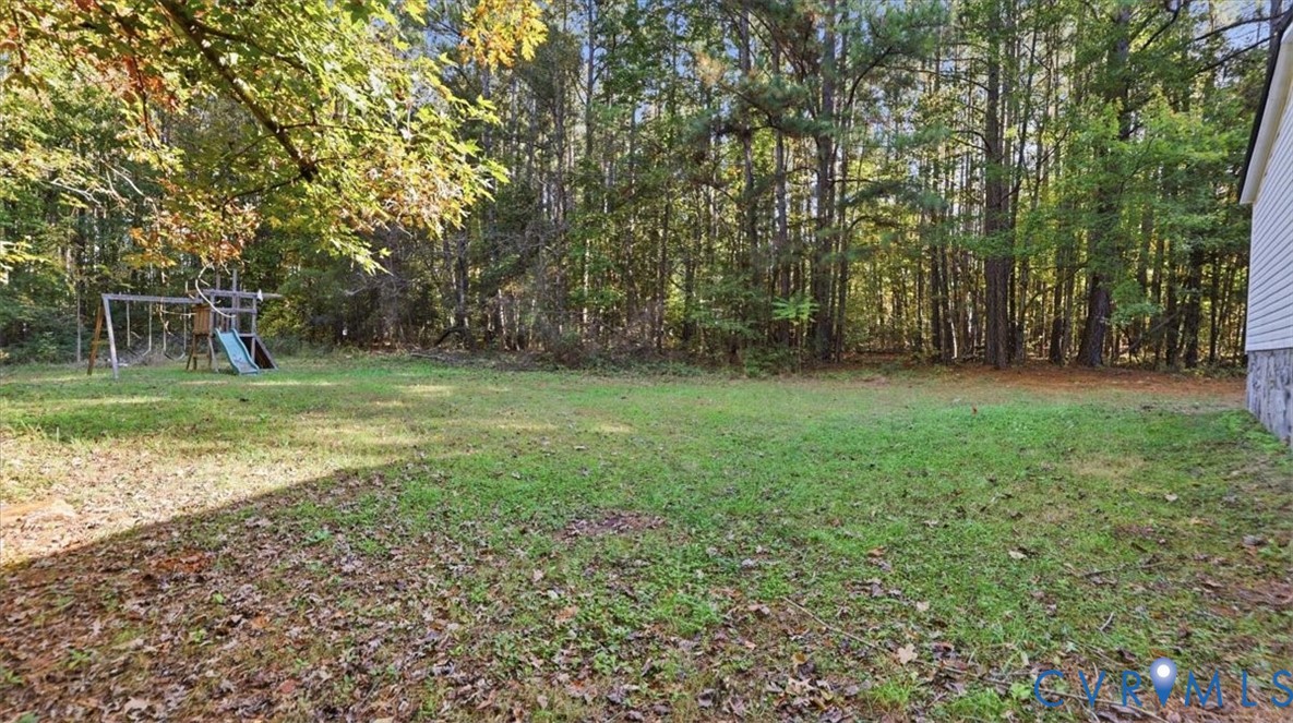 Expansive backyard featuring a large grass lawn, mature trees, and a wooded perimeter
