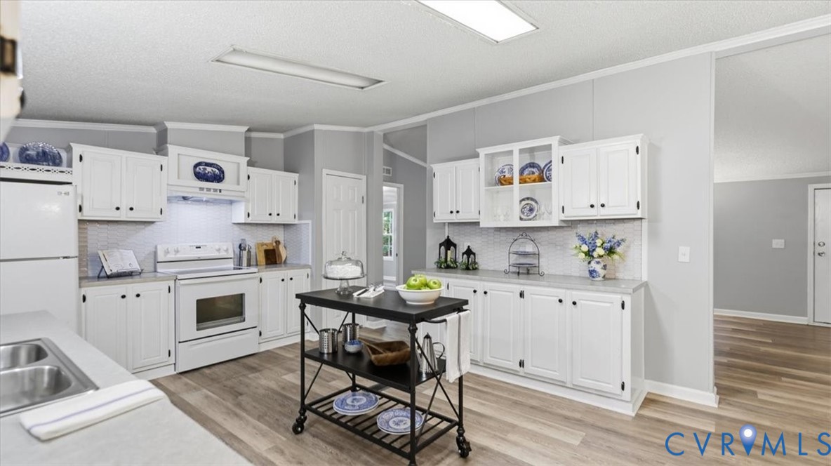 Kitchen featuring white cabinetry with glass-front display uppers, light-toned countertop surfaces, wood-finish flooring, and integrated range hood Kitchen featuring white cabinetry with glass-front display uppers, light-toned countertop surfaces, wood-finish flooring, and integrated range hood